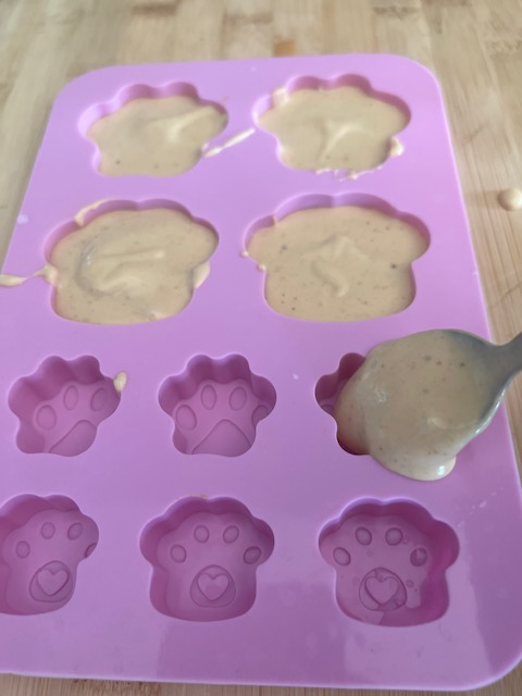 peanut butter mixture being poured into silicone dog treat molds