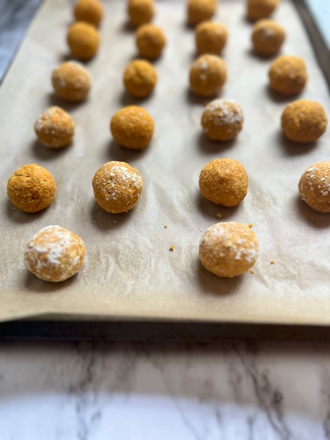 pumpkin and peanut butter dog treats rolled into small balls on parchment lined baking sheet